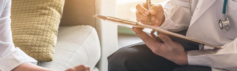 Two people sit opposite each other. One of them is holding a clipboard and writing some notes.