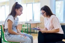 A teenage girl is speaking to an older woman. She is holding a clipboard and writing down notes.