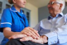 A nurse rests her hand on a patient's old hand.