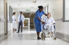A hospital corridor, with hospital staff and a patient in a wheelchair