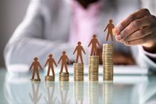 Wooden people standing on increasingly large piles of money.