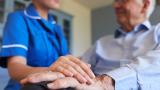 A nurse rests her hand on a patient's old hand.