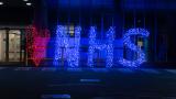 NHS in bright blue lights in the evening.