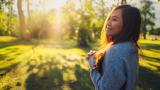 Person enjoying green space outdoors, surrounded by trees and sunlight.
