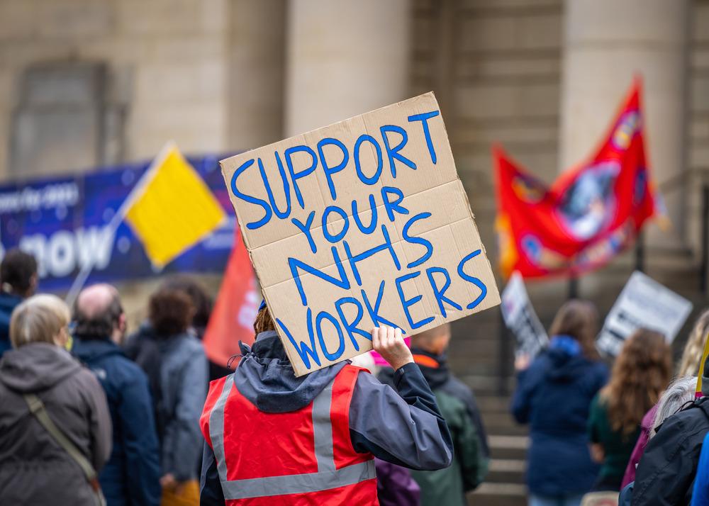 A group of people striking holding signs saying 'Support your NHS workers.'