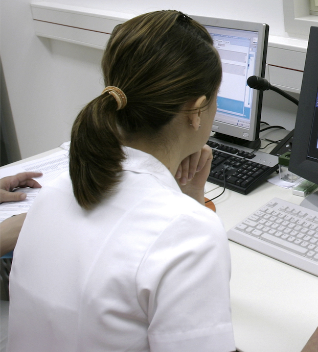 A person in a white coat looking at a computer screen.