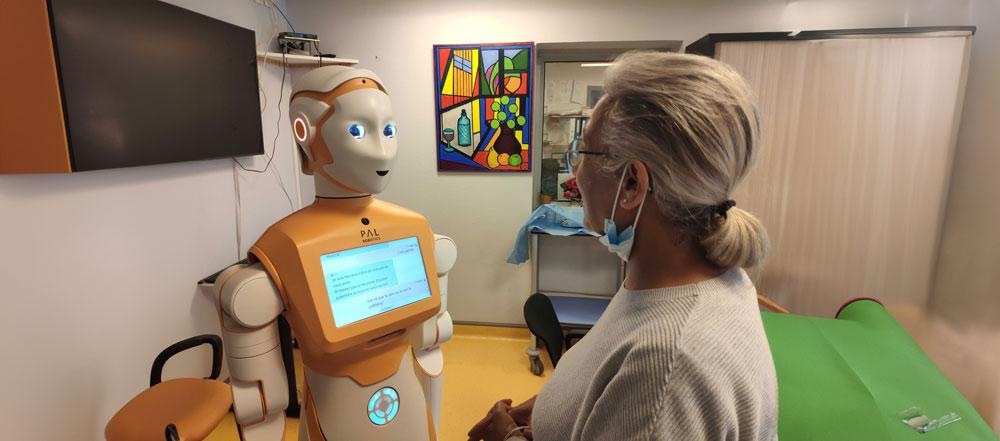 An orange robot called Ari speaks to a white woman.